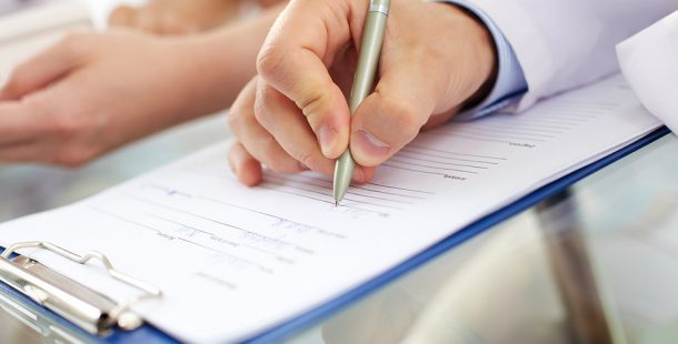 Hand Holding Pen to Paper on Clipboard